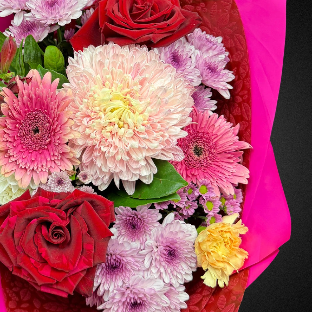 Close-up of premium bright roses, chrysanthemums, and carnations with pittosporum foliage in The Mum's Embrace Bouquet for Mother's Day.
