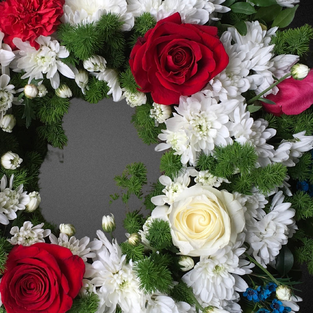 Close-up of a handcrafted wreath showcasing delicate pink roses, yellow chrysanthemums, and red carnations with lush green foliage.