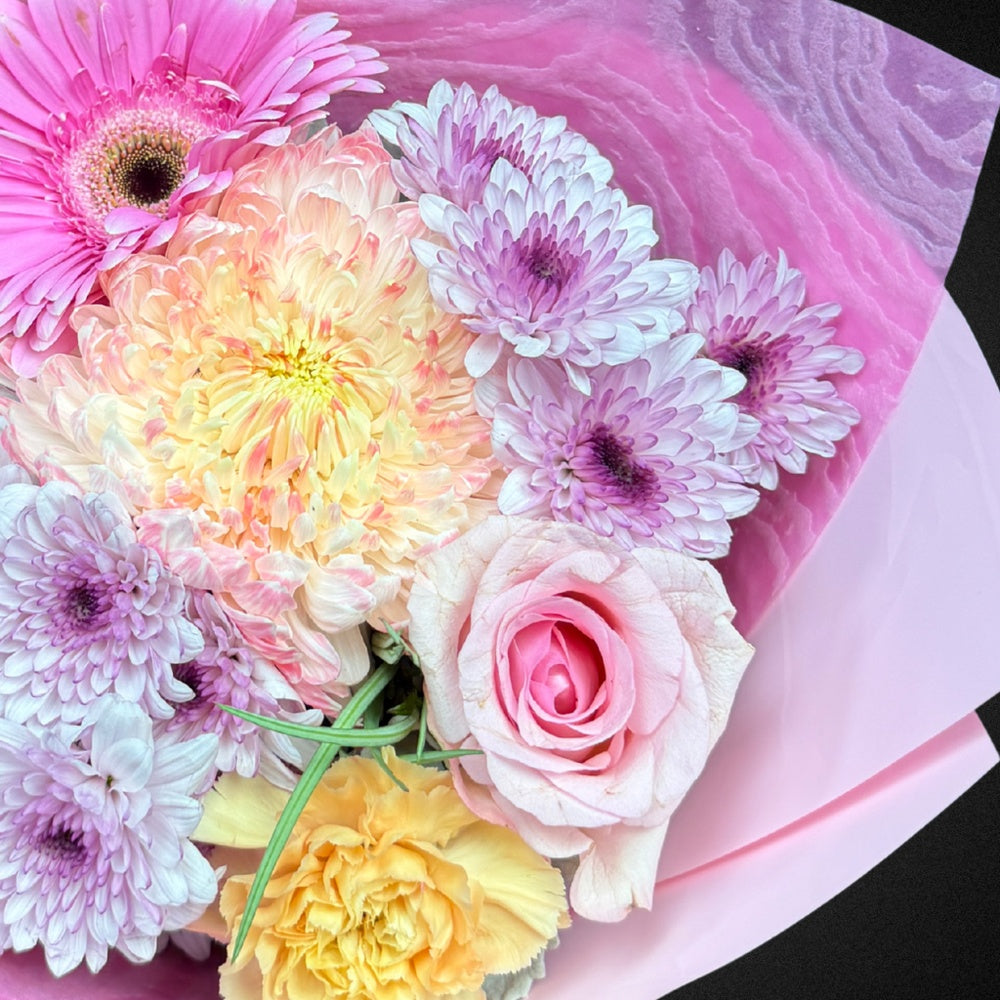 Close-up detail of 'The Everlasting Embrace' Mother's Day arrangement, showcasing the delicate textures of a soft pink rose, a creamy chrysanthemum, and the silvery hue of Dusty Miller foliage.