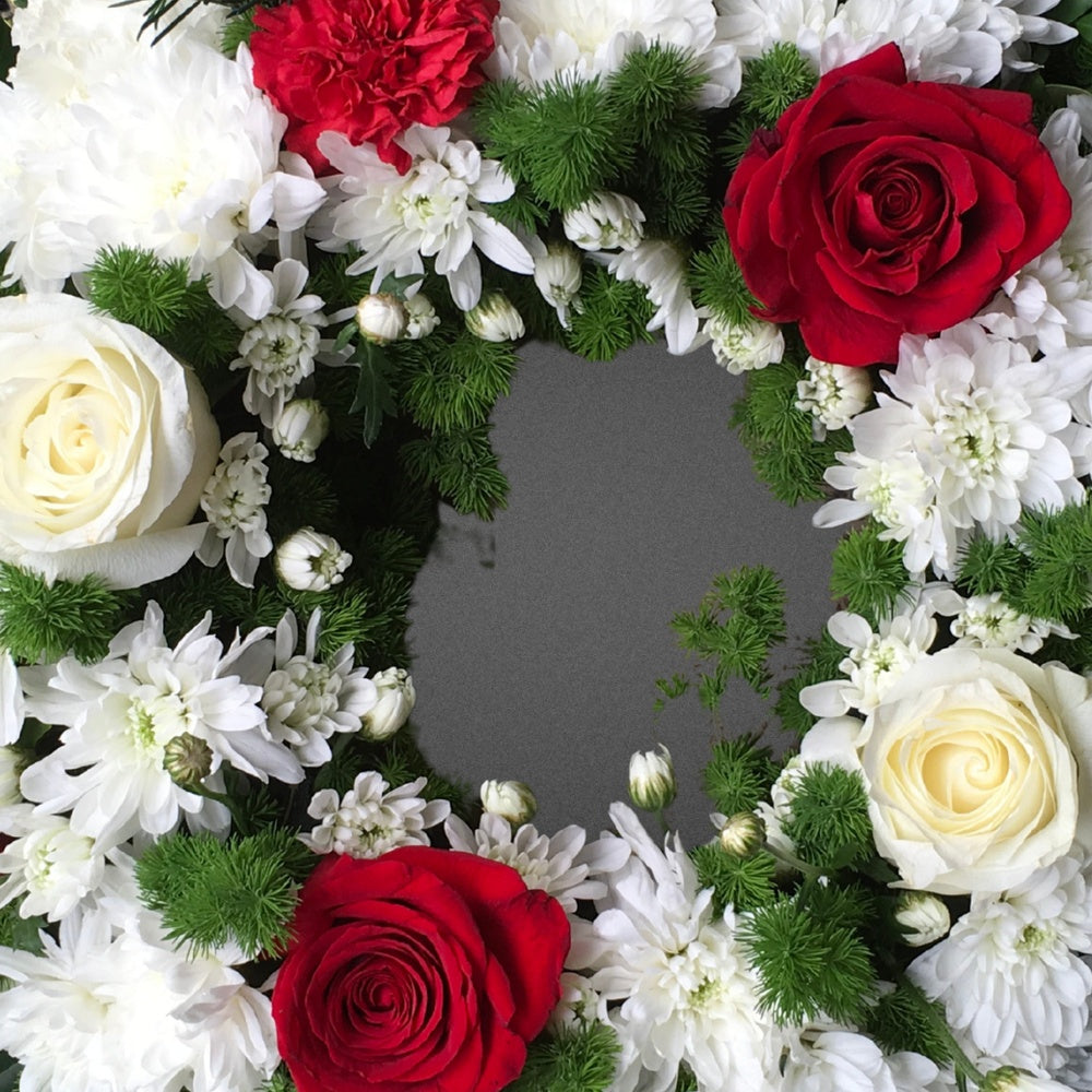 Close-up of a handcrafted wreath showcasing delicate pink roses, yellow chrysanthemums, and red carnations with lush green foliage.